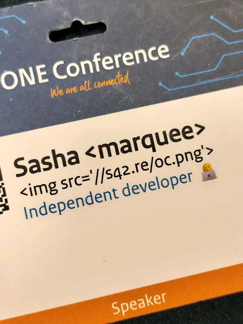A ONE Conference speaker badge in a lanyard holder, with the name line reading `Sasha <marquee><img src='//s42.re/oc.png'>` and a Speaker ribbon along the bottom.